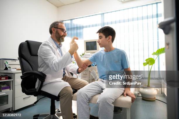 junge bewegt seinen arm mit hilfe eines arztes - orthopädie stock-fotos und bilder
