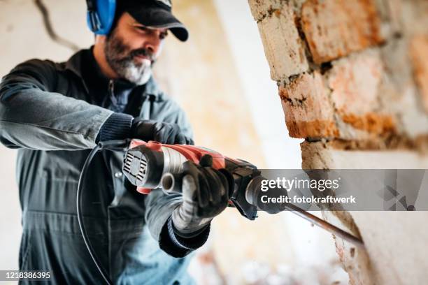 trabajador masculino demoliendo pared con taladro en casa - herramienta eléctrica fotografías e imágenes de stock