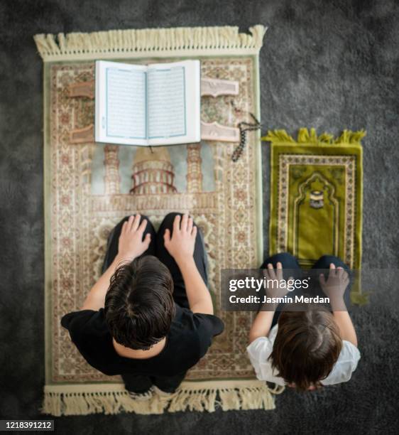 muslim family in living room praying and reading koran - american muslims celebrate eid al fitr with prayers foto e immagini stock