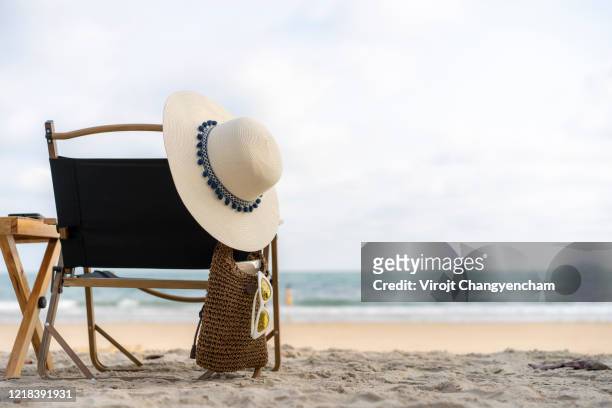 white weave hat and sunglass in the small weave bag hanging on beach chair with tropical beach scene - beach bag stockfoto's en -beelden