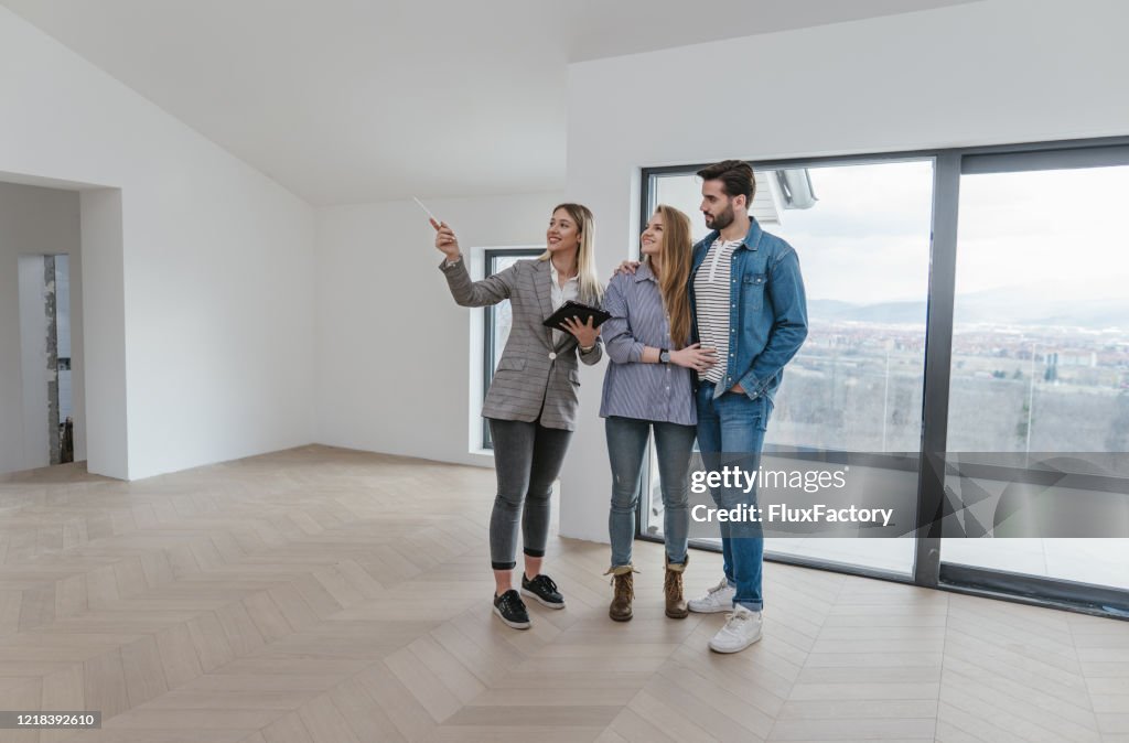 Weibliche Immobilienmaklerin zeigt eine Wohnung zum Verkauf an ein junges Paar