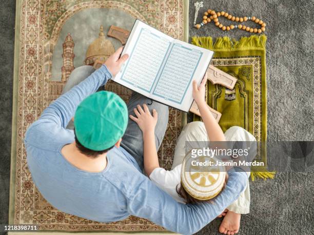 muslim family in living room praying and reading koran - koran stock-fotos und bilder