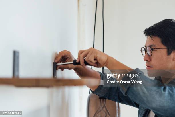 young man fixing a shelf with screwdriver at home - building shelves stock pictures, royalty-free photos & images