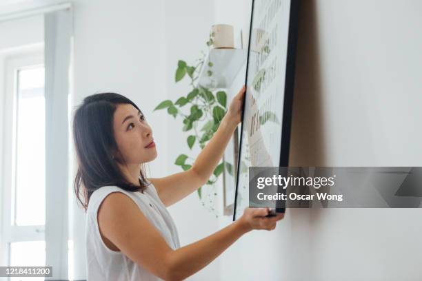 young woman hanging picture frame on wall - hanging picture frame stock pictures, royalty-free photos & images