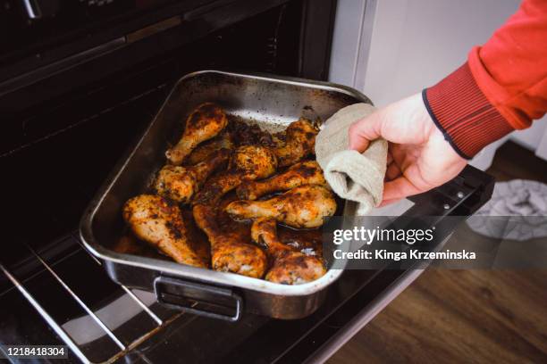 getting the roasting tray out of the oven - chicken drumsticks stockfoto's en -beelden