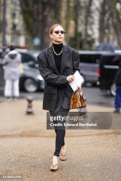 Pernille Teisbaek wears sunglasses, a black turtleneck pullover, a golden chain necklace, a gray striped oversized blazer jacket, a brown snake...