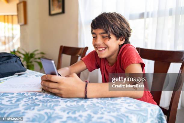 cute latinx hispanic boy smiling while texting on smartphone at home - 12 year old cute boys stock pictures, royalty-free photos & images