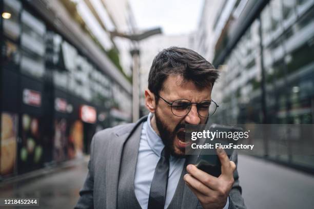 young distraught businessman shouting while recording a voicemail on a mobile phone - shouting phone stock pictures, royalty-free photos & images