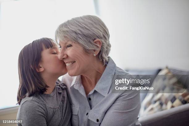 nette kleine enkelin küssen aufgeregt großmutter auf wange - child whispering stock-fotos und bilder