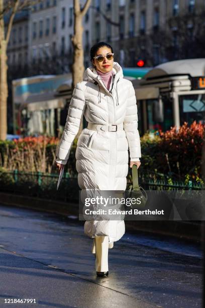 Caroline Issa wears a pale purple turtleneck top, a white long puffer coat with a hood, a green leather bag, Ray-Ban sunglasses, outside Lanvin,...