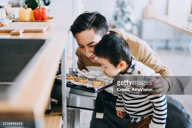 father with son baking cookies together in the kitchen and smelling freshly baked cookies straight from the oven. stay at home self isolation during the covid-19 health crisis - man baking cookies stock pictures, royalty-free photos & images