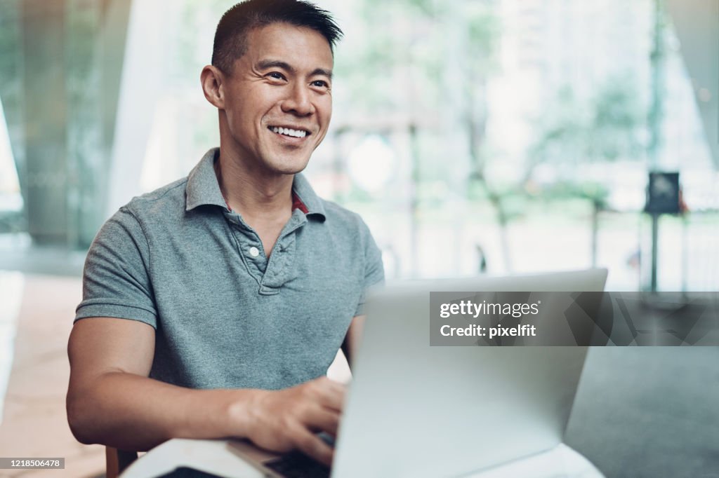 Hombre de etnia asiática sonriente con computadora portátil en café