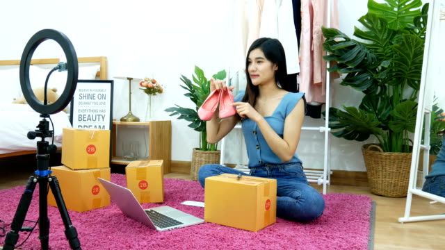 4K. Asian woman live streaming for selling shoe, fashion accessories online on social media via mobile phone from bedroom at home. owner of small business working from home during self isolation