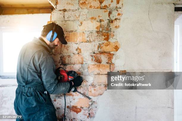 trabajador maduro demoliendo pared con taladro en casa - reforma assunto fotografías e imágenes de stock