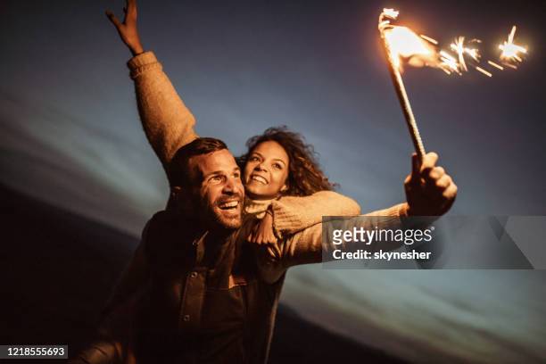carefree couple having fun with flaming torch at night. - flaming torch stock pictures, royalty-free photos & images