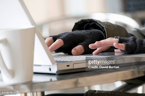 young male using laptop computer keyboard wearing fingerless gloves - fingerless glove stockfoto's en -beelden
