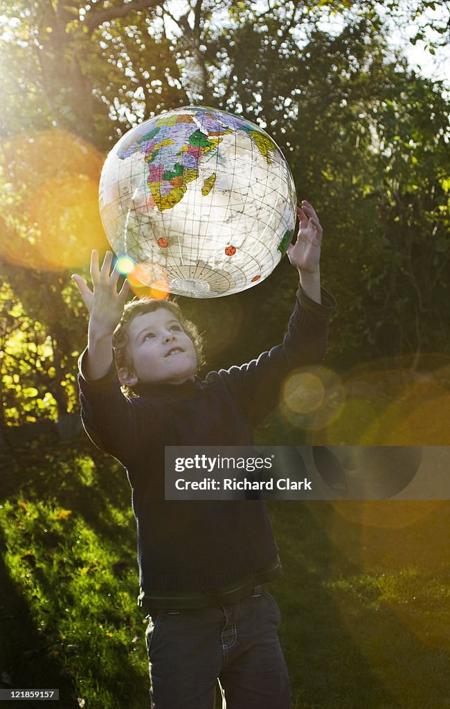 Boy (6-8 years) playing with transparent plastic globe in garden, UK