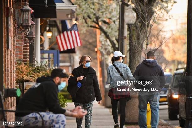 Babylon Village, N.Y.: People wearing masks stroll Main St. In Babylon Village as the sun sets, Wednesday, April 8, 2020. .