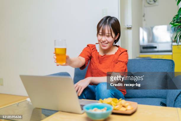 young woman meeting her loved ones via video conference and drinking beer together - acquaintance via the internet stock pictures, royalty-free photos & images