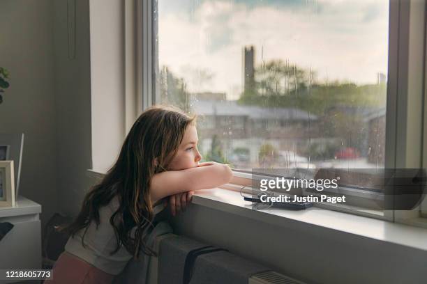 young girl looking out of window on a rainy day - pandemic illness stock-fotos und bilder