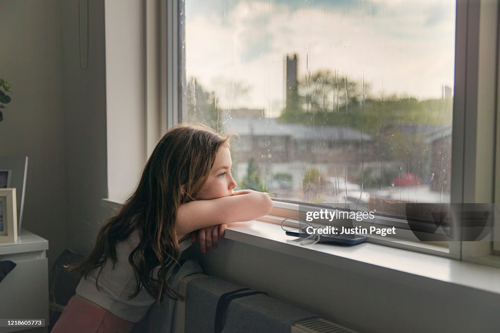 Young girl looking out of window on a rainy day