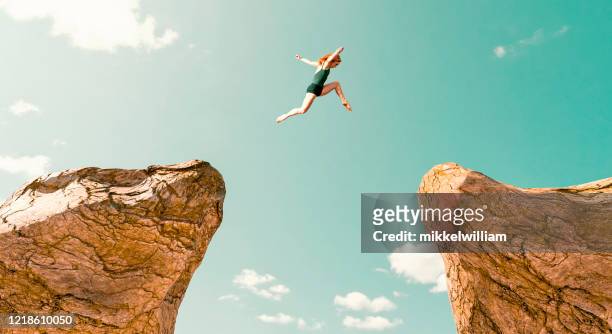woman makes dangerous jump between two rock formations - positive emotion stock pictures, royalty-free photos & images