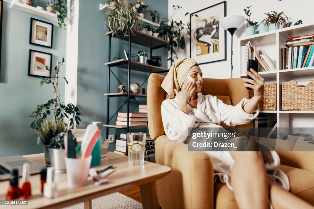 Mature woman talking to friend over voice call during beauty treatment at home
