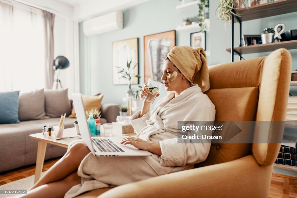 Woman putting beauty mask and teleconferencing with friends due to social distancing measures