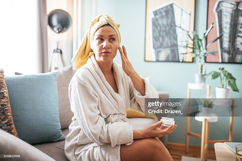 De rijpe vrouw past gezichtsmoisturizer en schoonheidsmasker op haar gezicht toe