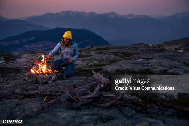 female camper making bonfire on top of mountain. - warming up stock pictures, royalty-free photos & images