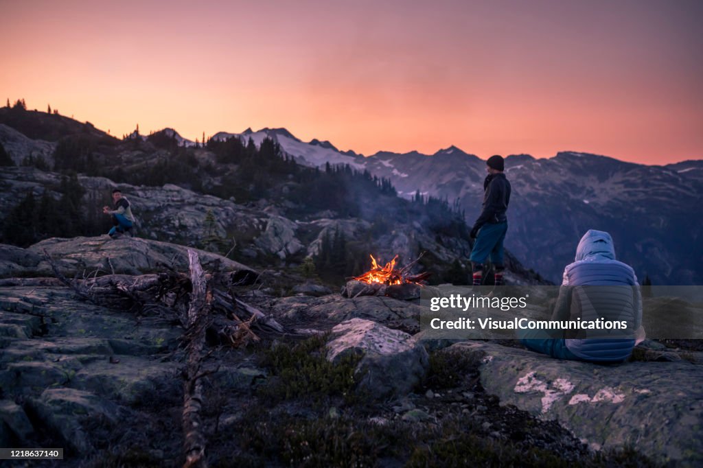 Friends near campfire on top of mountain at dusk.