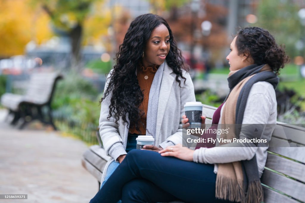 Pregnant woman talking with female friend while relaxing on park bench