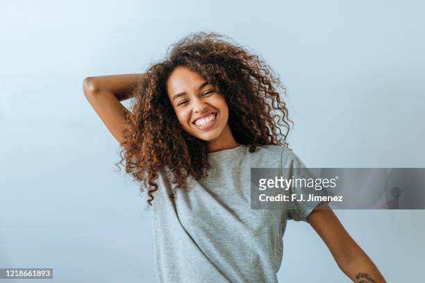 portrait of woman with afro hair smiling with white wall background - person gemischter abstammung stock-fotos und bilder