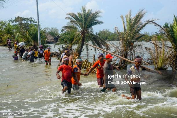 People are seen crossing a flooded road as the embankment of the coastal area was broken after the landfall of cyclone Amphan. Thousands of shrimp...