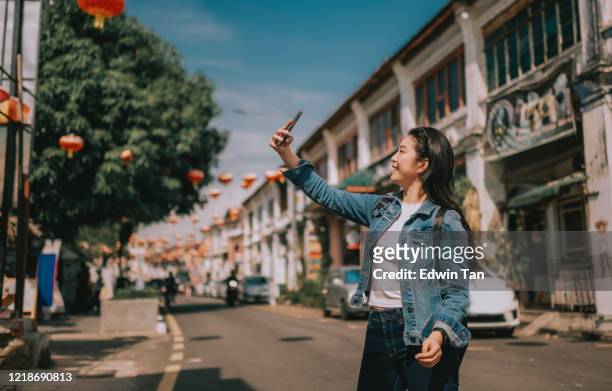 a young asian chinese girl tourist in penang, malaysia , south east asia taking photo in the street with her mobile phone - penang stock pictures, royalty-free photos & images