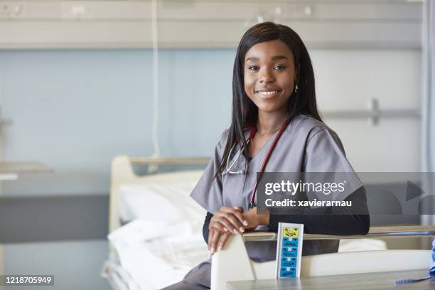 portret van glimlachende afrikaanse verpleegsterzitting op het bed van het ziekenhuis - korte mouwen stockfoto's en -beelden