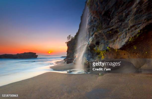 beautiful sunset at melasti beach, bali indonesia with sunset at waterfall near the beach. - melasti ceremony in indonesia stock pictures, royalty-free photos & images