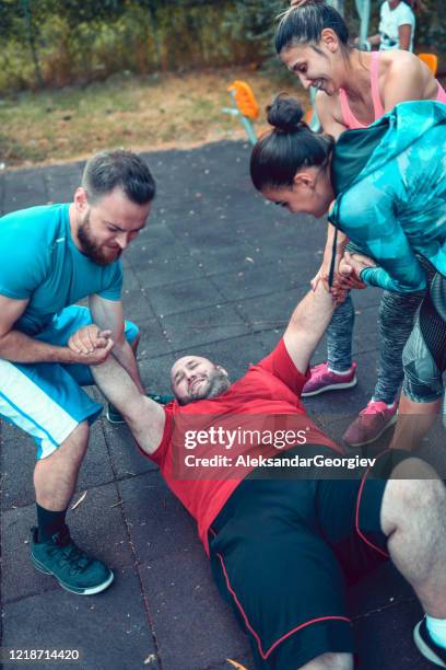 friends helping their tired overweight friend get up after training - fat man lying down stock pictures, royalty-free photos & images