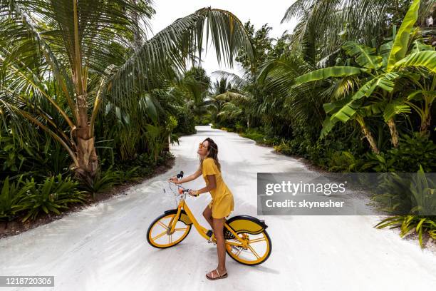 mulher feliz se divertindo em uma bicicleta na natureza. - yellow dress - fotografias e filmes do acervo