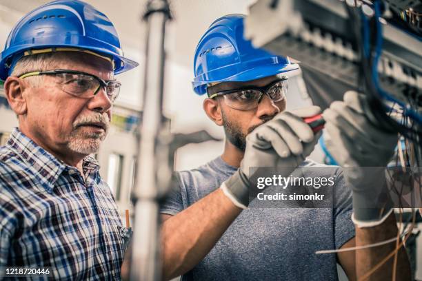 männlicher lehrling, der drähte in der verteilertafel verbindet - elektriker stock-fotos und bilder