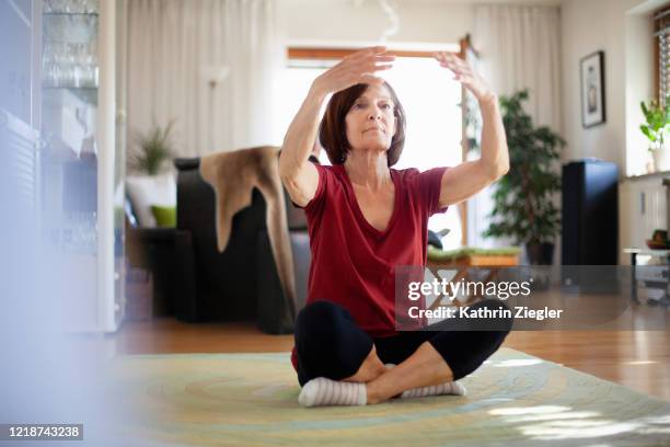 senior woman doing relaxation exercises at home - sitting on ground stock-fotos und bilder