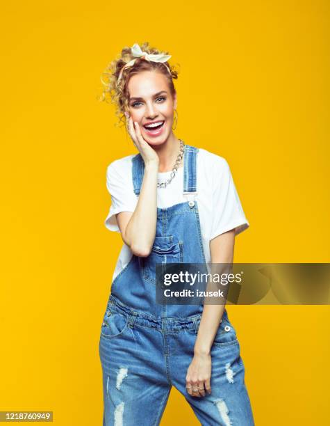 porträt einer glücklichen jungen frau in coveralls auf gelbem hintergrund - jeans latzhose frau stock-fotos und bilder