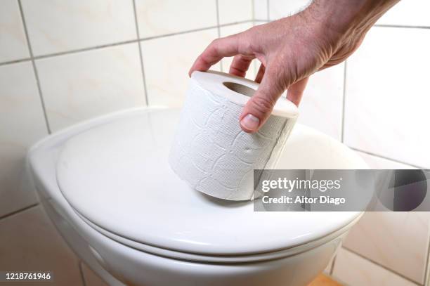 man's hand taking a roll of toilet paper which is on the toilet bowl. germany. - hemorrhoid - fotografias e filmes do acervo