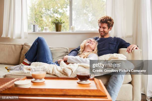 young couple talking while relaxing on their living room sofa - cobertor imagens e fotografias de stock