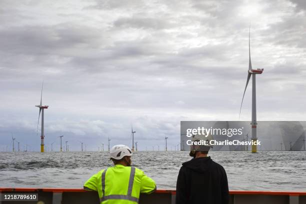 två tekniker står på överföring fartyg däck och på morgonen och tittar på havsbaserad vindkraftpark och offshore plattform runt - wind turbines bildbanksfoton och bilder
