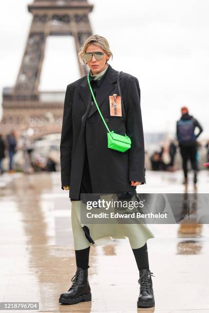 Guest wears mirror sunglasses, a black oversized blazer jacket from Wooyoungmi, a neon green crossbody bag, a dress, black leather shoes, outside Ann...