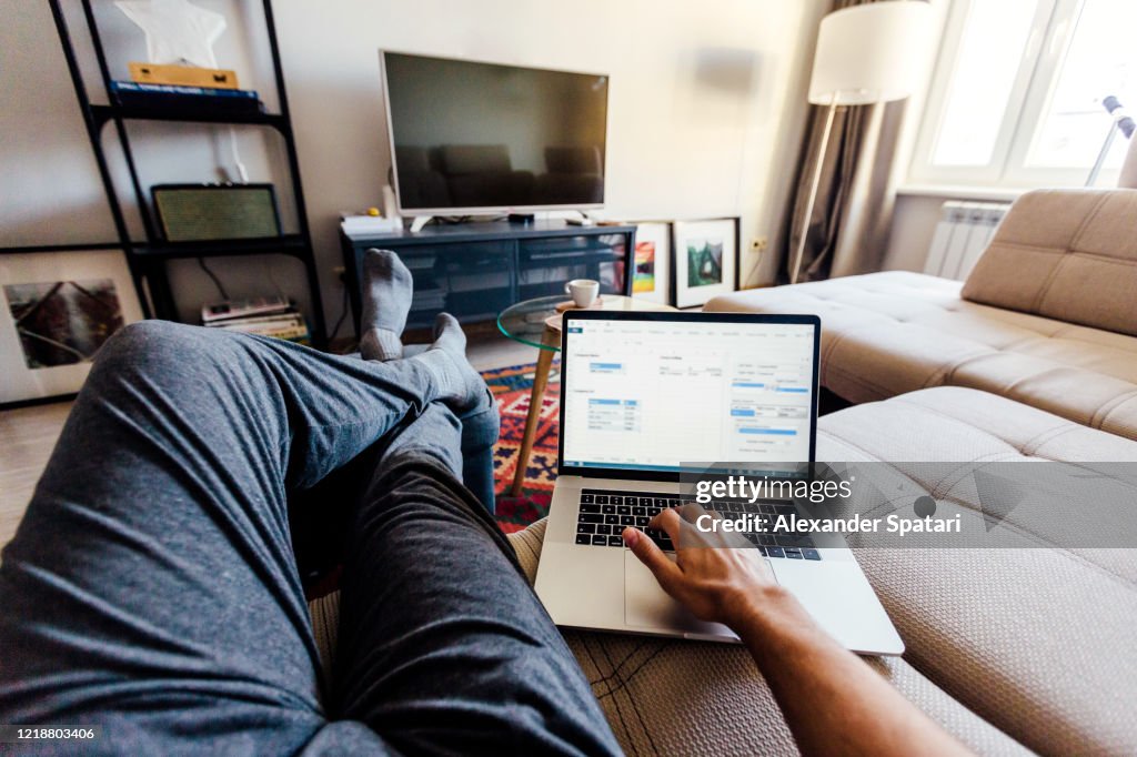 Personal perspective point of view of a man working on laptop in the living room at home