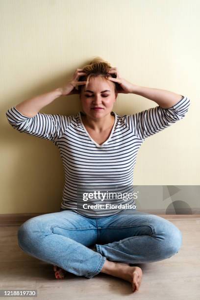a middle-aged woman sitting in a yoga pose at home on a sofa in casual closes  with laptop and meditating - fat massage stock pictures, royalty-free photos & images