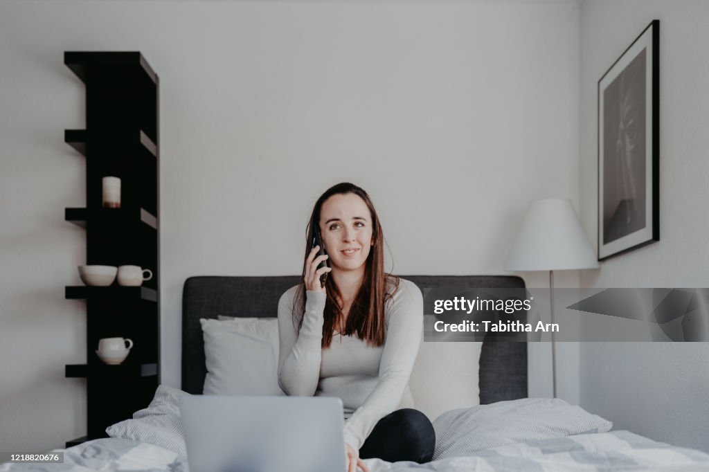 Frau arbeitet von zu Hause im Home Office im Bett und telefoniert