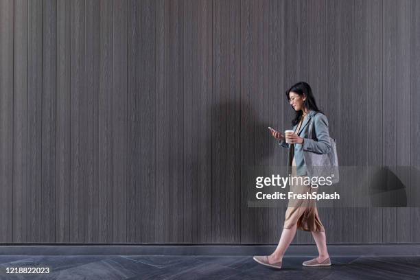 young asian businesswoman walking on the street and texting on her mobile phone, copy space - wide angle city stock pictures, royalty-free photos & images